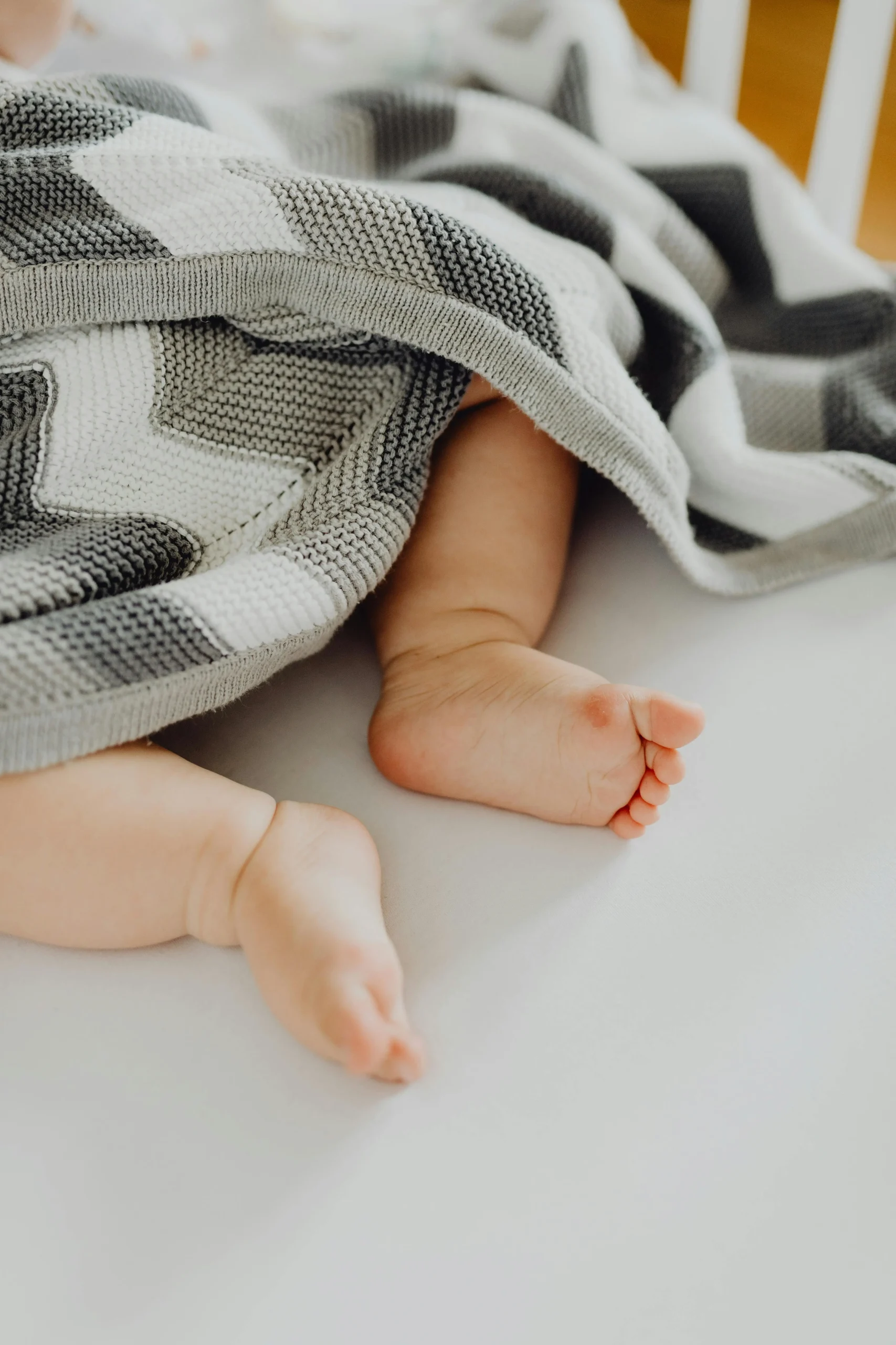 Close-up of baby feet peeking out from under a soft knitted blanket while sleeping in a crib
