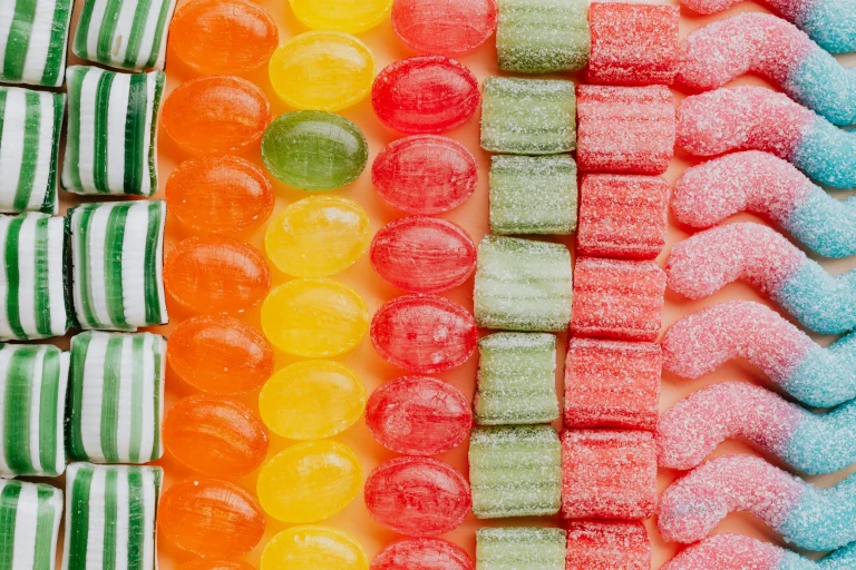 Assorted colorful candies arranged in neat rows, including striped, gummy, and sugar-coated sweets