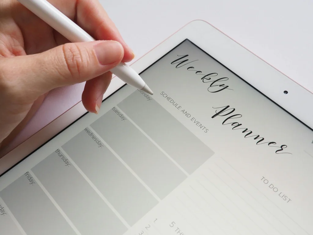 A person using a stylus to write on a digital weekly planner displayed on a tablet