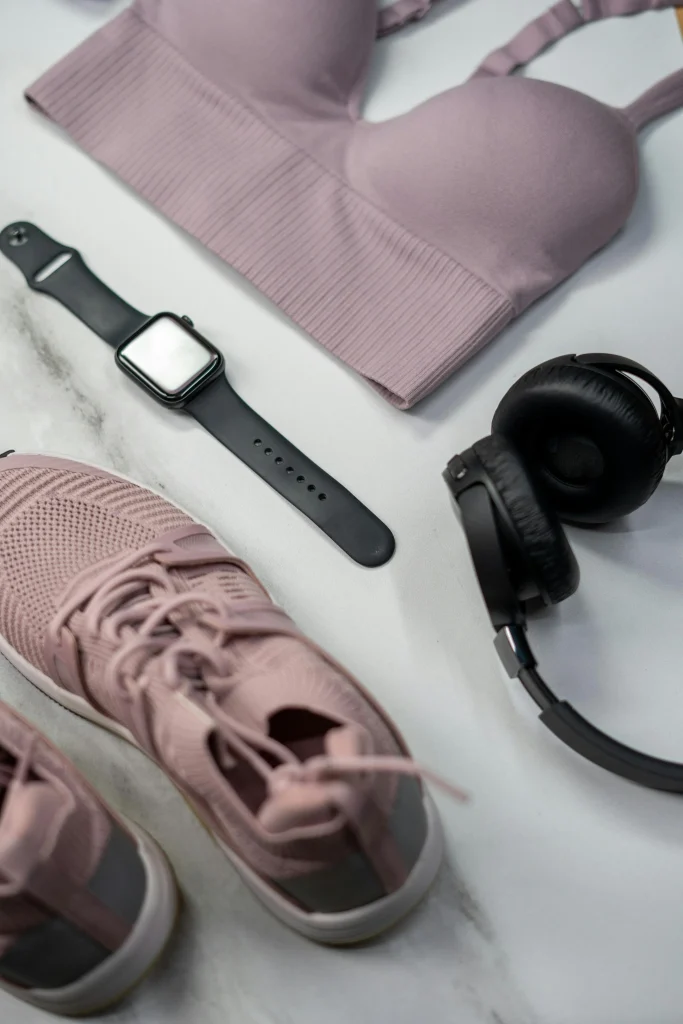 Flat lay of pink sports bra, matching sneakers, smartwatch, and headphones for fitness and workouts