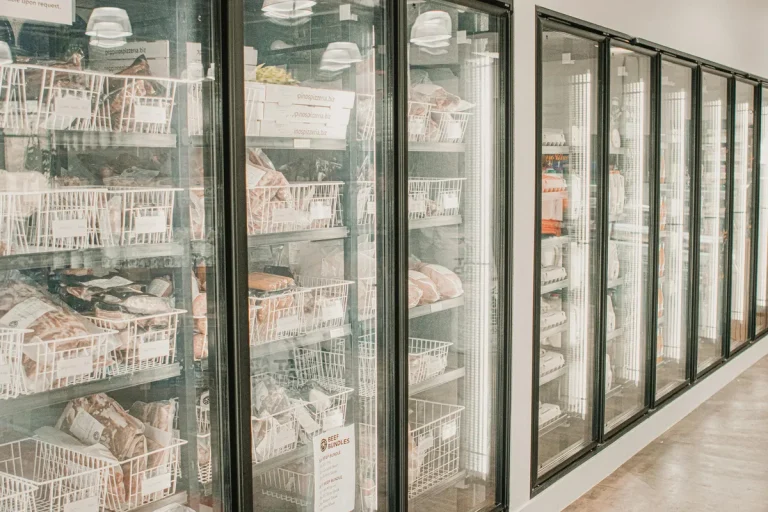 Large commercial freezer with glass doors showing baskets of packaged frozen meats and food products.