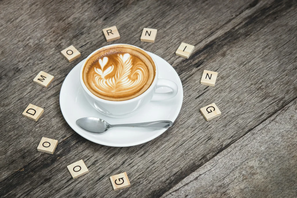 Cup of coffee with latte art on wooden table, surrounded by Scrabble tiles spelling Good Morning