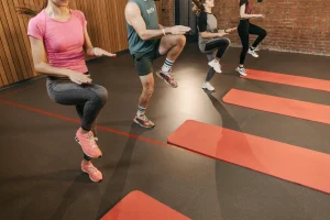 Group of people performing high knee exercises on red mats during an indoor fitness class