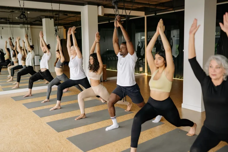 Diverse group of people practicing warrior pose in a yoga studio with arms raised overhead