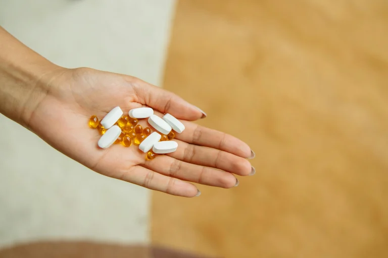 Hand holding oval white tablets and round yellow capsules over a soft beige background