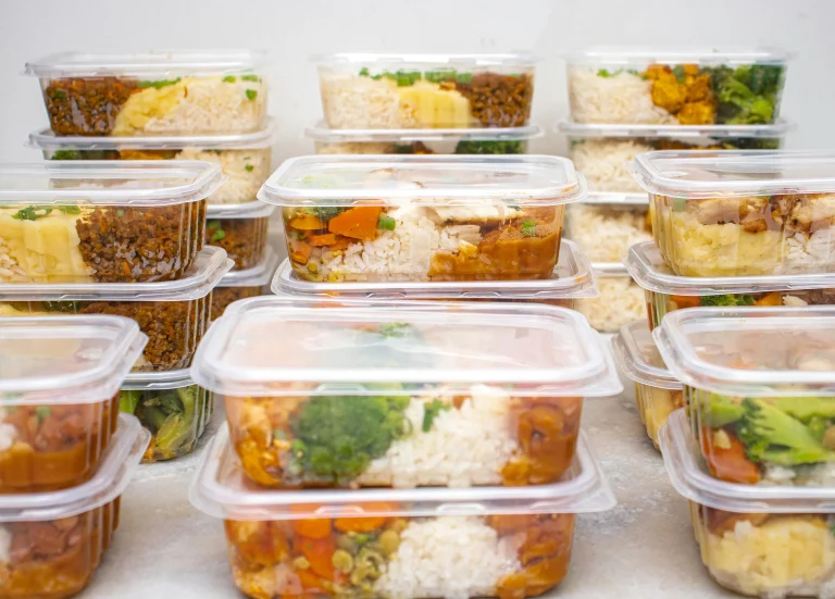 Stacked plastic containers filled with meal prep portions of rice, vegetables, and protein for healthy eating