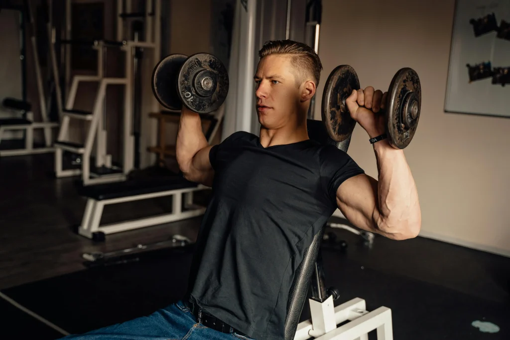 Man lifting dumbbells overhead in shoulder press exercise at gym