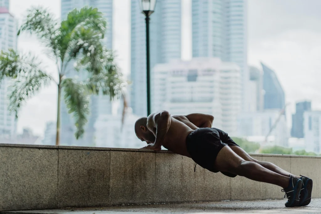 Shirtless man performing incline push-ups on a concrete ledge with city buildings in the background
