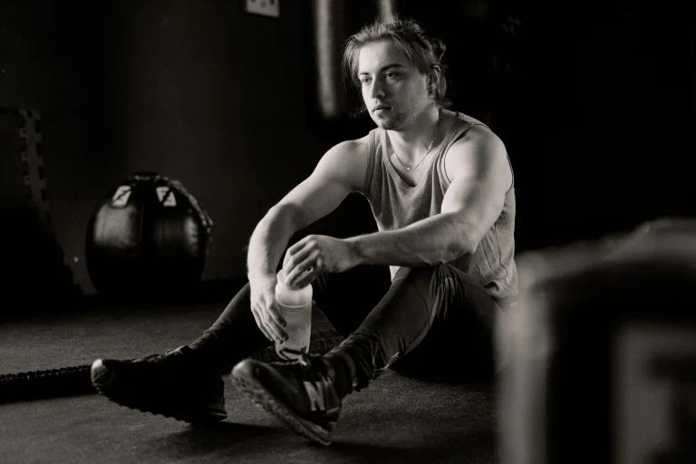 Athletic man sitting on gym floor holding water bottle after workout