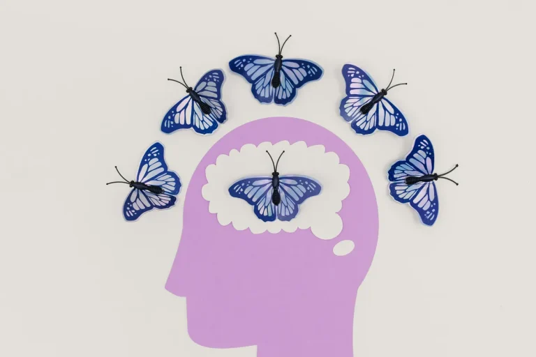Illustration of a purple human head silhouette with blue butterflies surrounding and inside the brain area, symbolizing mental health and positive thoughts.