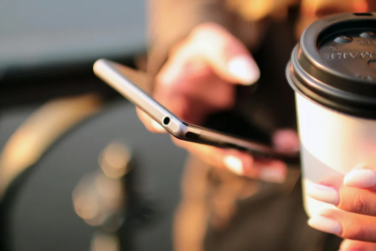 Close-up of a person holding a coffee cup and smartphone outdoors