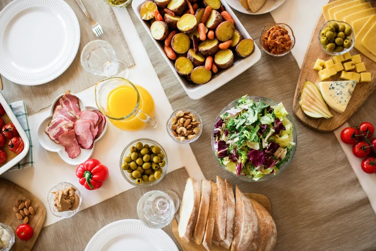 Well-arranged brunch table with salad, roasted vegetables, cheeses, bread, cold cuts, and fresh juice