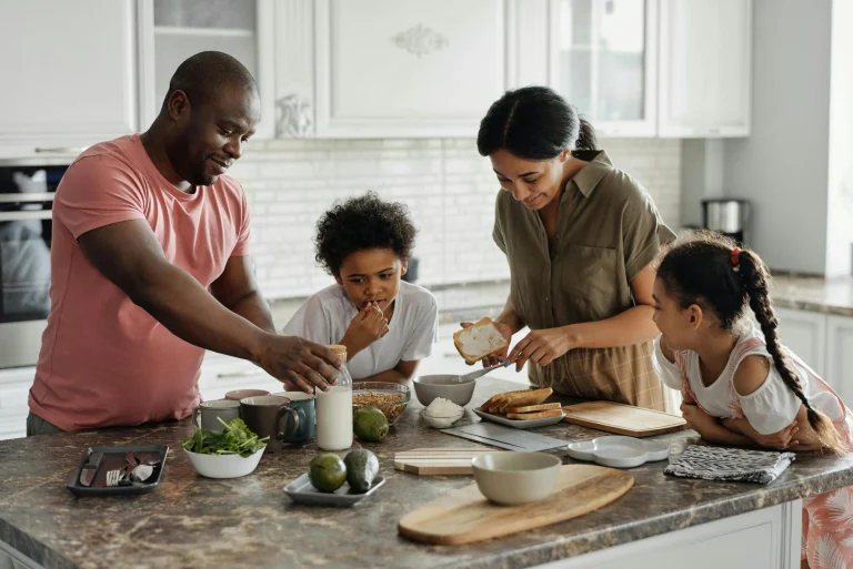 Two adults and two children preparing food together in a bright kitchen with fresh ingredients