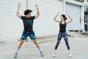 Man and woman exercising together outdoors doing jumping jacks in athletic wear