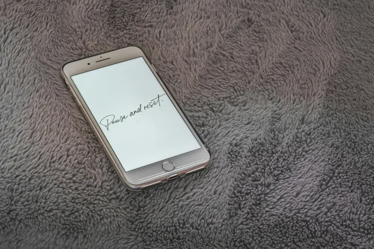 Smartphone on a gray blanket with screen text “Pause and reset” promoting mindfulness and relaxation.
