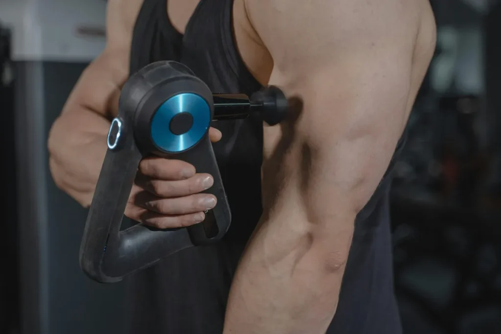 Close-up of a man using a massage gun on his arm muscles for recovery