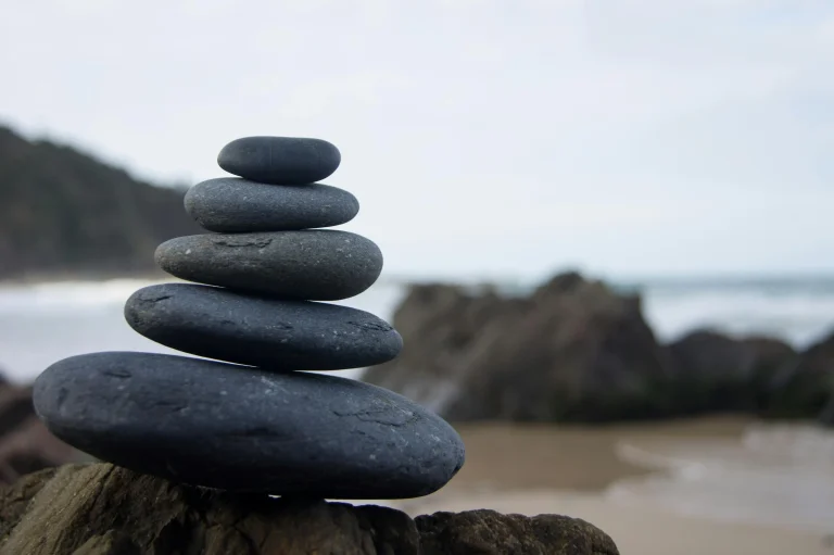 Stacked black stones balanced on the beach, symbolizing calm, balance, and mindfulness with RealFit Wellness.