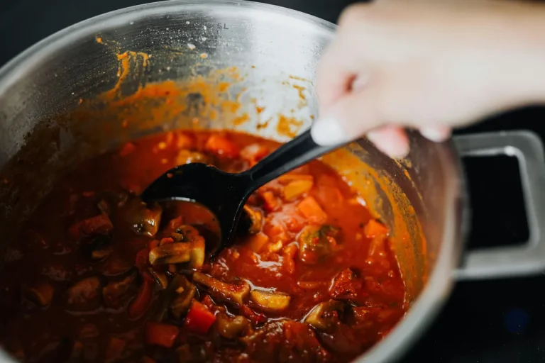 Close-up of a pot with simmering vegetable stew being stirred with a black ladle.