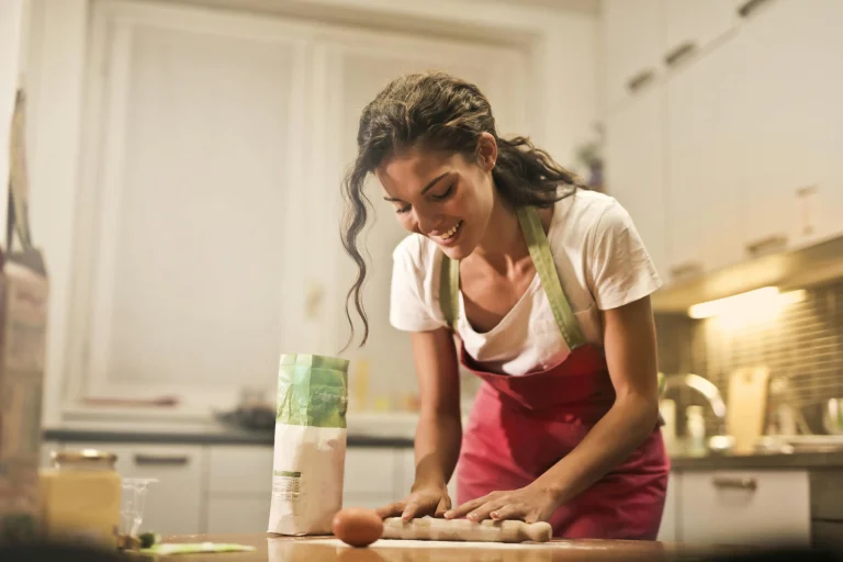 Smiling woman in apron rolling dough on kitchen counter