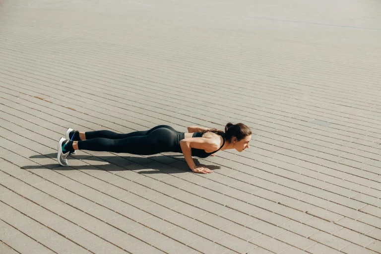 Young woman performing push-ups outdoors on a paved surface in athletic wear