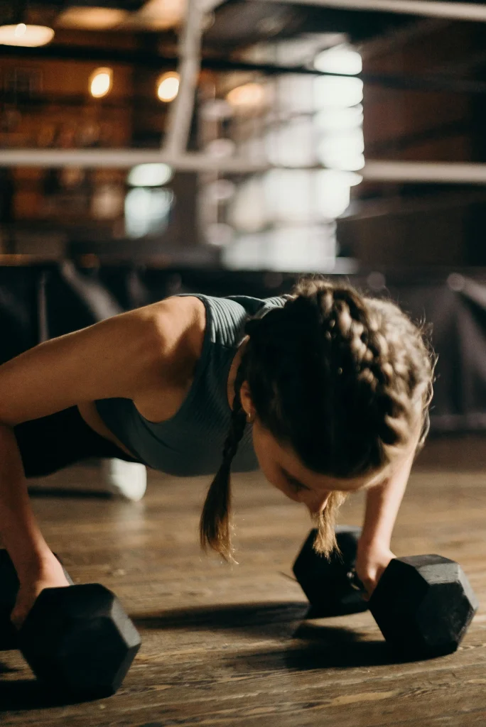 A woman performing push-ups with dumbbells in a gym, building strength and endurance