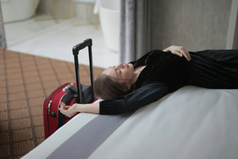 Woman resting on bed with suitcase.webp