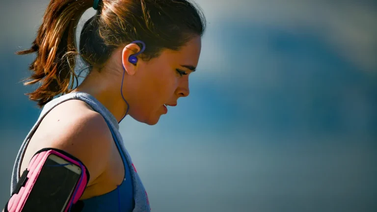Close-up of a woman jogging outdoors with blue earphones and a phone armband, looking focused