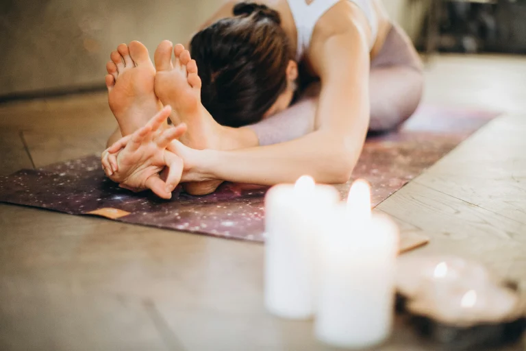 Woman practicing yoga stretch on mat with candles for relaxation