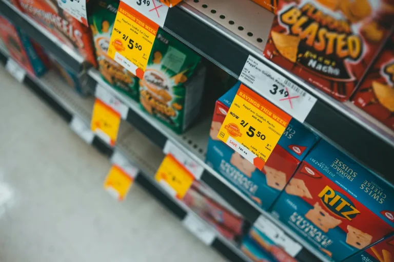 Close-up of supermarket snack aisle showing boxes of crackers and chips with bright yellow sale price tags.