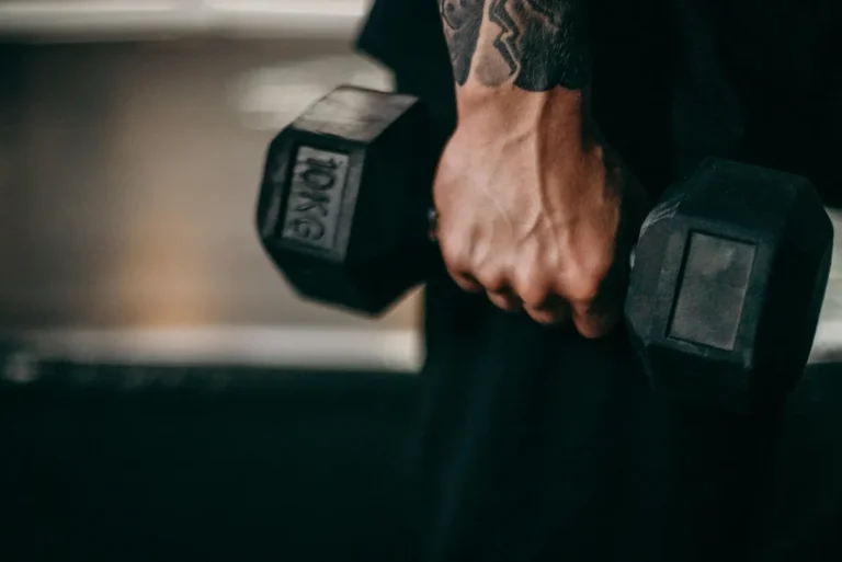 Person gripping black hex dumbbells with tattooed forearm during strength workout