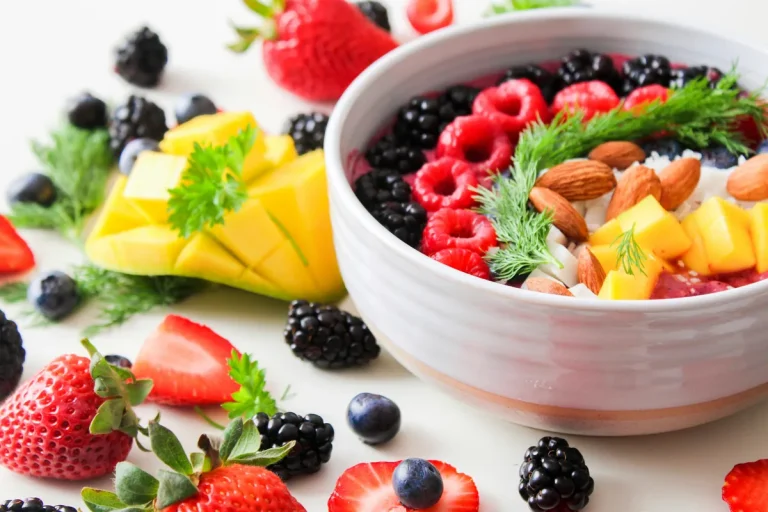 Vibrant bowl of fresh berries, mango, almonds, and herbs on white surface