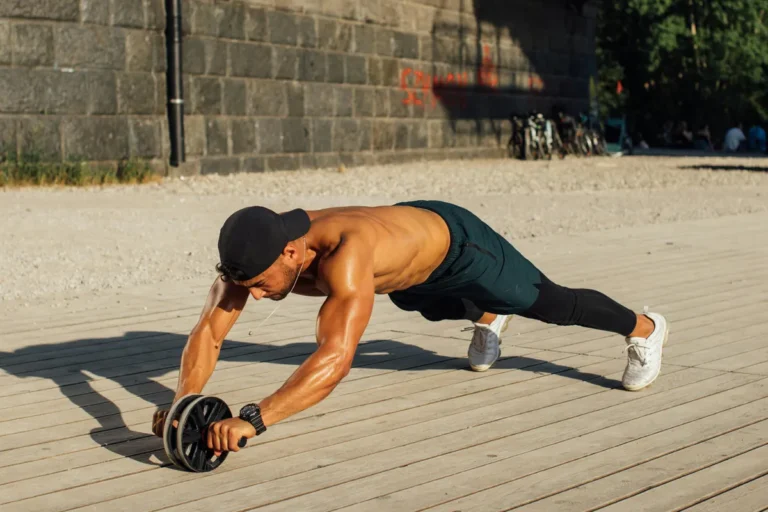 Shirtless man using ab roller on wooden deck in public outdoor fitness space