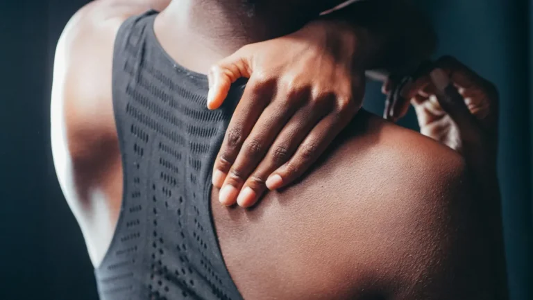 Close-up of person in black athletic top massaging sore shoulder to relieve post-workout tension